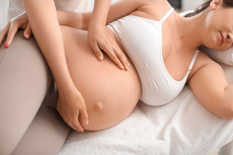 Eine schwangere Frau liegt auf der linken Seite, ihr Bauch wird von zwei Händen massiert.